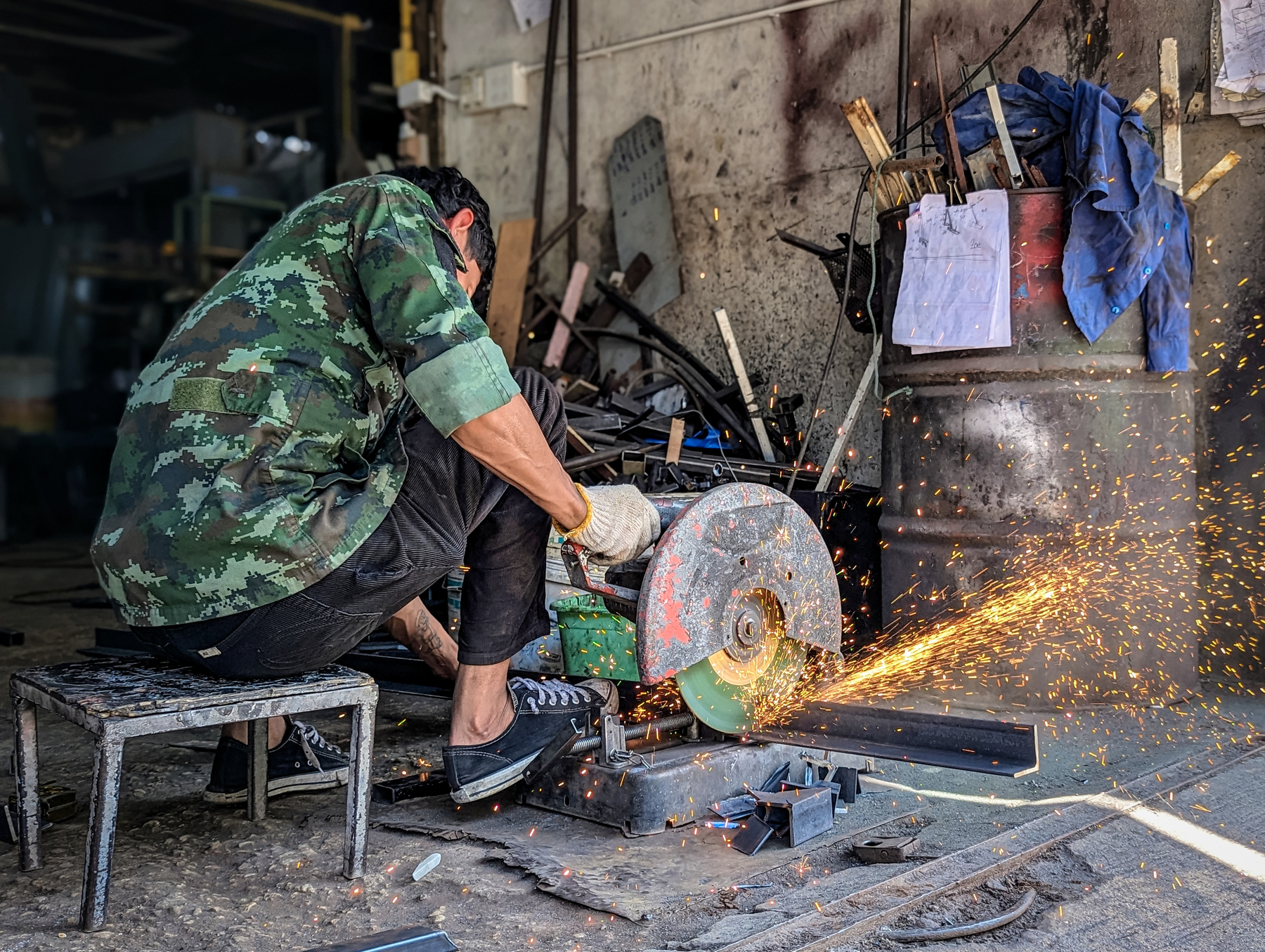 Auto-generated description: A person in a camouflage jacket operates a metal grinder in a workshop, producing bright sparks.